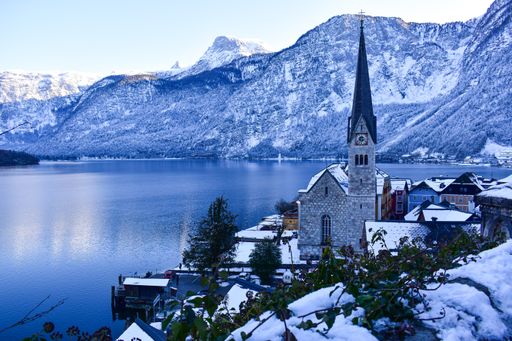 picture of a small village with a beautiful church situated in the middle of the mountains next to a lake during wintertime