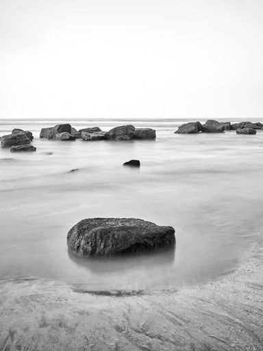 A vertical shot of stones washed by the long exposure seascape in grayscale