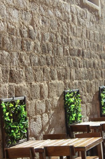 A vertical shot of wooden tables and chairs by a wall made of stones on a sunny day in Croatia
