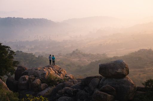 An aerial shot of a mountainous region with big rocks and cliffs with two people looking at the view