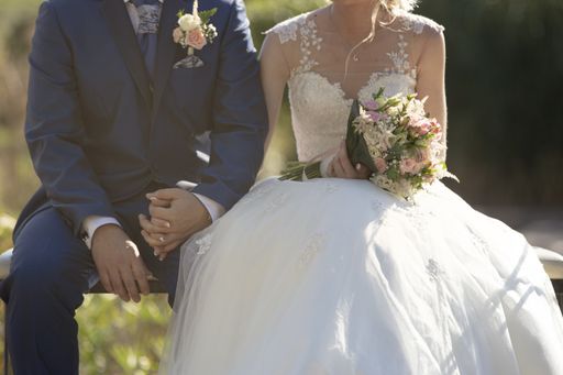A closeup shot of a newlywed couple sitting on a bench while holding hands with each other during the wedding