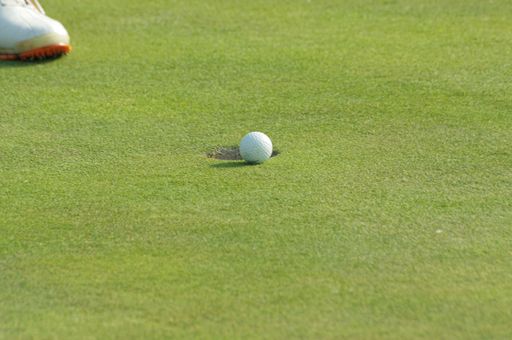 The golf ball on the grass with a few centimeters left to fall into the hole