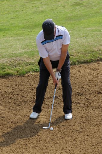 A vertical shot of a Caucasian man playing golf on a bunker
