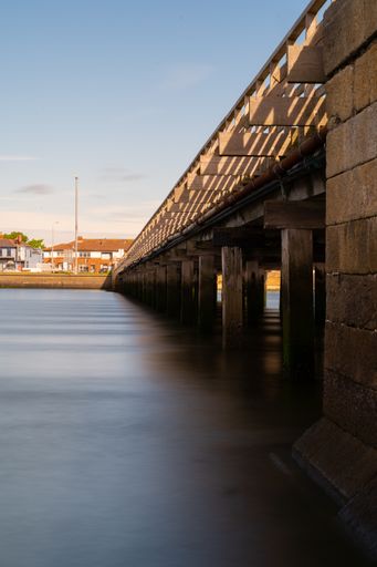 A closeup of a long brick bridge over a river under a blue sky
