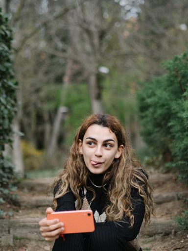 A closeup portrait of a teenage girl tanking selfies on her phone with her tongue out