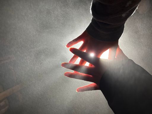 A vertical shot of a person's hands aimed at the sky covering the sunlight
