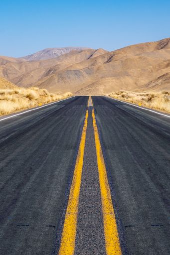 A vertical perspective shot of an empty highway in the background of mountains.
