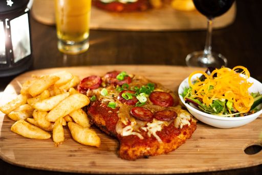 A chicken parma with chips and salad on a wooden plate with beer and wine