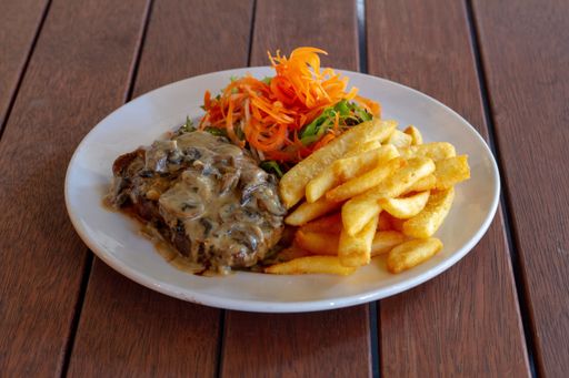 A closeup shot of steak with chips and salad on a white plate on wooden table