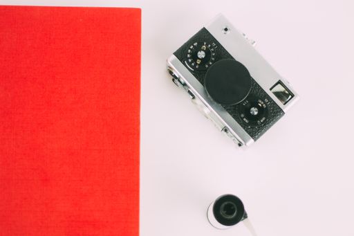 A top view of an red book beside a vintage camera with a film roll on a white surface