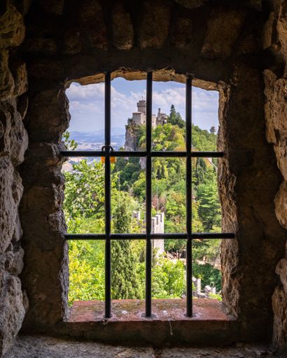 A photo of a castle rusted jail window and a view of De La Fratta, from Guaita fortress, San Marino