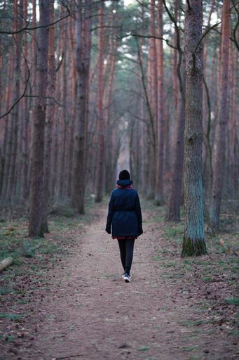 A vertical shot of a woman in warm winter clothes walking in a forest during the daytime
