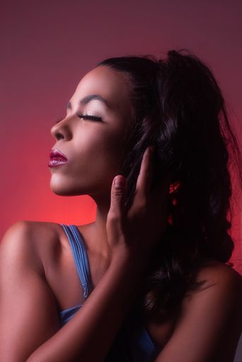 A vertical shot of a young Hispanic brunette woman with red lipstick posing eyes closed on the red background