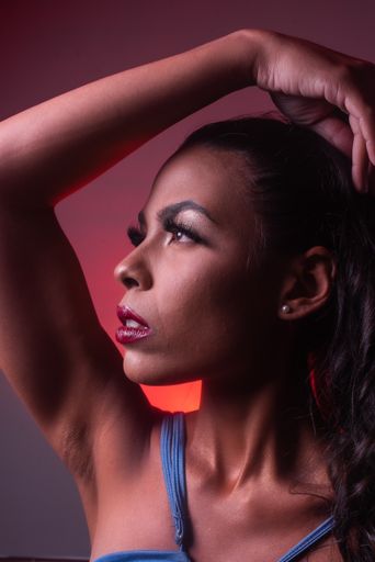 A vertical shot of a brunette Hispanic woman with red lipstick and blue dress looking at the right side