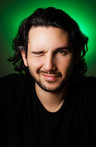 A portrait of a handsome Caucasian male with one eye closed on the green background