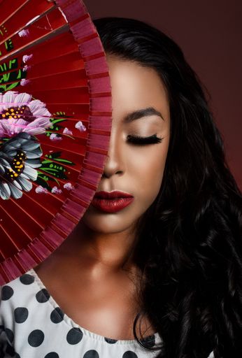 A vertical shot of a Hispanic female part of the face covered with a  handheld folding fan