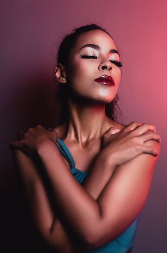 A vertical shot of a young Hispanic woman hugging herself on the red background