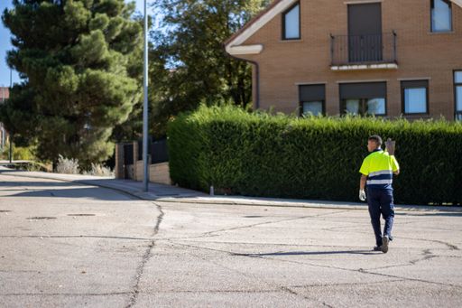 A back view of a young male gardener with a hoe tool crossing the street