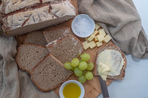 A top view of a whole grain sourdough bread with sliced cheese and grapes on a wooden board on top of a marble table