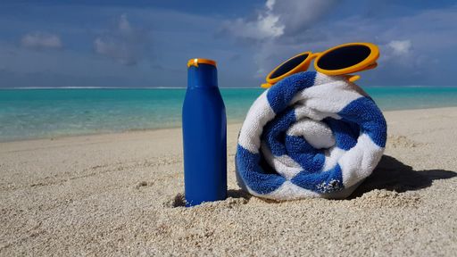 A closeup shot of sunscreen, a towel, and sunglasses on the beach