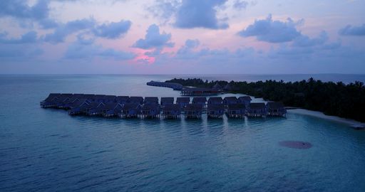 An aerial beautiful view of seascape surrounded by cabins and  growing trees in Maldives during sunset