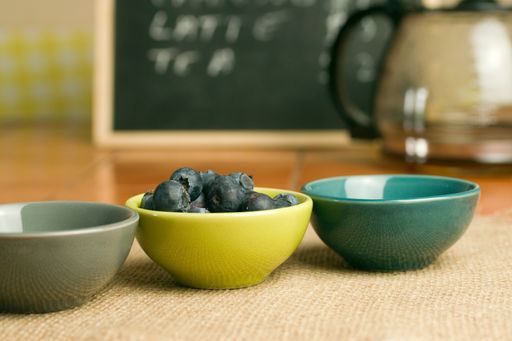 A closeup shot of a bowl of blueberries near empty bowls on a wooden surface