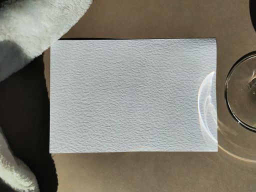 A top view closeup of a napkin on a table next to a glass and a white fabric