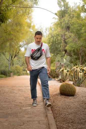 A caucasian model wearing a Gucci bag and a white Nasa t-shirt posing in a public park