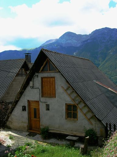 A vertical shot of a countryside house under the cloudy sky against mountains covered with forest