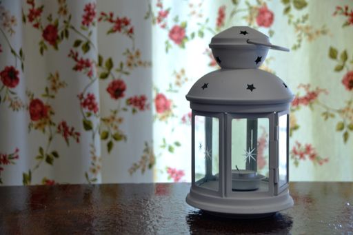 A closeup of a decorative white lantern with a candle against the curtain with floral pattern.