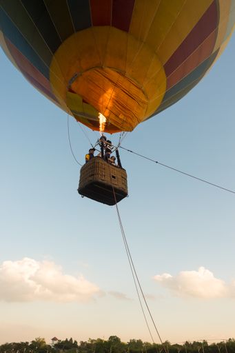 A low angle shot of a yellow hot air balloon flying near the green field ground with a blue sky