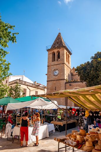 A Market in Son Servera with plenty of market stalls and people shopping, church in the background