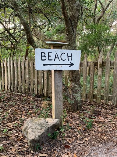 A vertical shot of a sign showing a direction of a beach