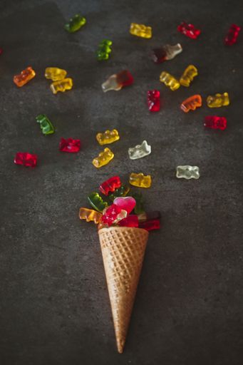 A vertical closeup shot of an ice cream cone with gummy bears on the dark surface