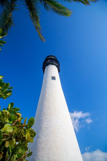 A low angle of the tall white painted lighthouse under the cloudy blue sky