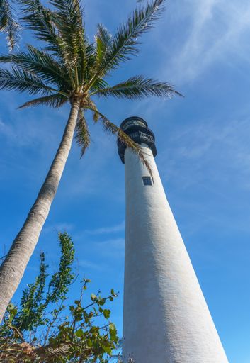 A low angle of the tall white painted lighthouse under the cloudy blue sky