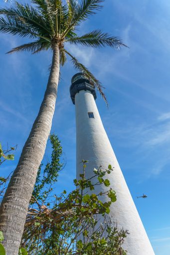 A low angle of the tall white painted lighthouse under the cloudy blue sky