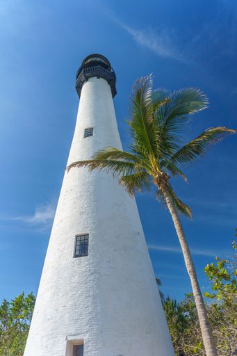 A low angle of the tall white painted lighthouse under the cloudy blue sky