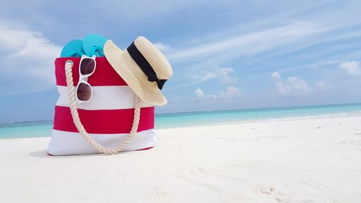A closeup shot of beach bag with slippers, hat and sunglasses on the sand beach