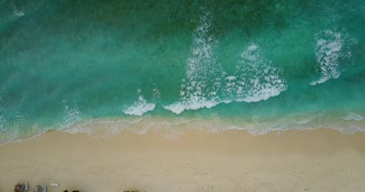 An aerial top view of a sandy beach against a turquoise sea on a sunny day