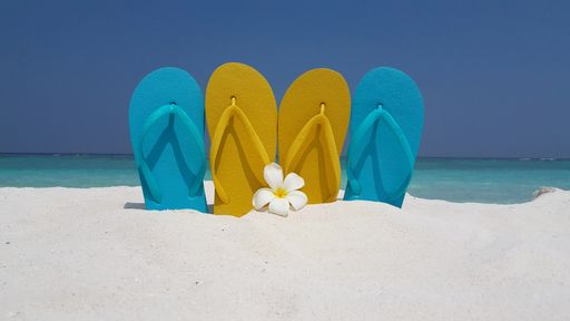 A closeup shot of two pairs of slippers on the sand in the Maldives