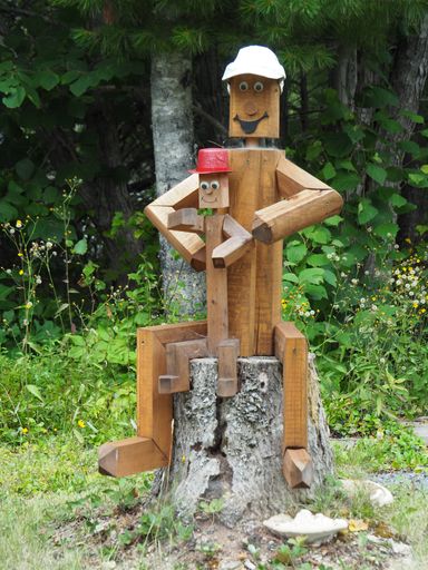 A closeup shot of a cute wooden carving with the form of toys surrounded by green trees during daytime