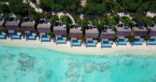 An aerial view of bungalows with swimming pools on sandy beach in Maldives