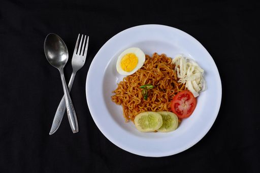A top view of spicy noodles with boiled egg and sliced vegetables on black background