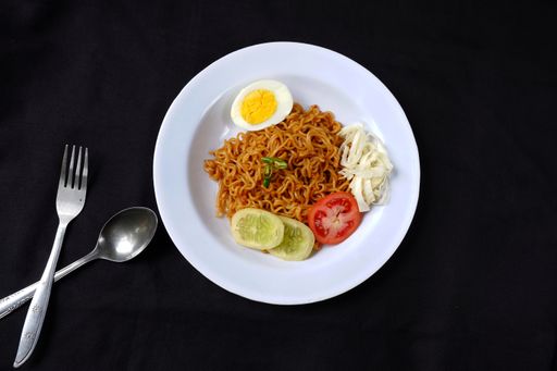 A top view of spicy noodles with boiled egg and sliced vegetables on black background