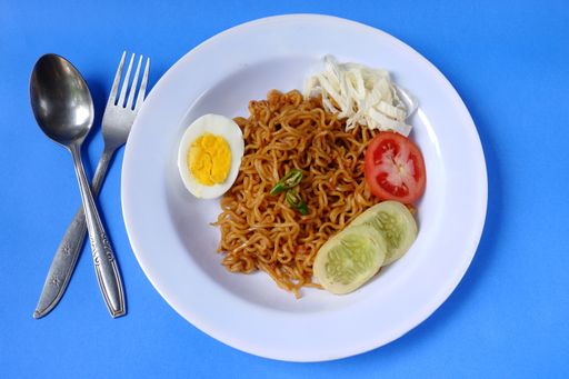 A top view of spicy noodles with boiled egg and sliced vegetables on blue background