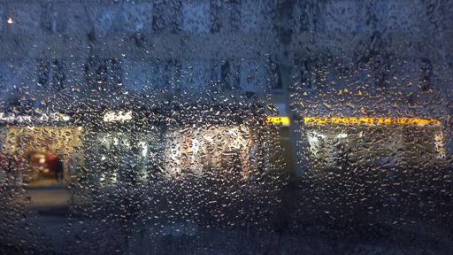 A closeup of the wet glass with the store lights in the background.