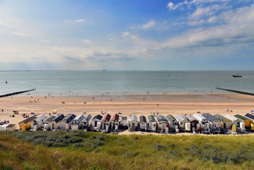 A high angle shot of a populated beach under the cloudy blue sky with beach houses in a row