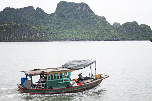 A fishing boat with people sailing on water near the mountains of Vinh Ha Long, Vietnam