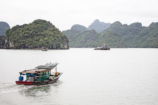 A beautiful shot of a small Fisher boat in the sea in Vinh Ha Long Vietnam with green mountains
